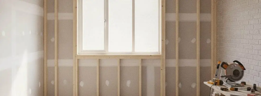 Un cantiere dentro casa: parete nuova con montanti in legno, muro in mattoni a vista e attrezzi sul banco.